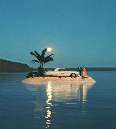 two people standing on an island in the middle of water with a car parked next to it