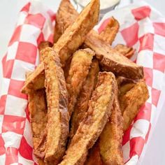 fried french fries on a red and white checkered paper in a basket with dipping sauce