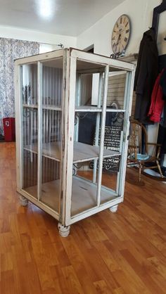 a glass cabinet sitting on top of a hard wood floor next to a wall clock