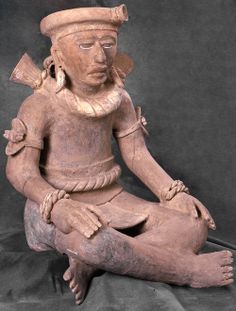 an old statue sitting on top of a black cloth covered floor next to a gray wall