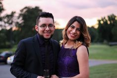 a man and woman standing next to each other in front of a parking lot at sunset