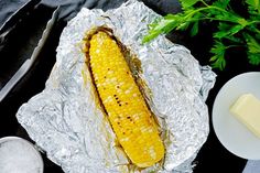 a grilled corn on the cob with butter and parsley next to it