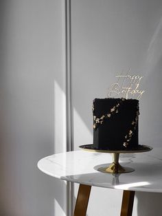 a black and gold birthday cake sitting on top of a white table next to a metal pole