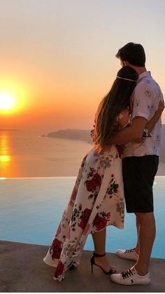 a man and woman standing next to each other in front of a pool at sunset