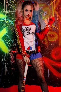 a woman dressed in costume holding a baseball bat and posing for a photo with graffiti on the wall behind her