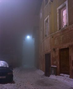 a car parked in the middle of a snow covered street with buildings on both sides