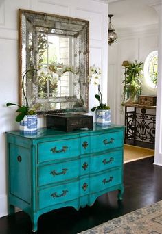 a blue dresser and mirror in a room with white walls, black flooring and wood floors