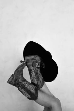 black and white photograph of a woman with gloves on her face wearing a cowboy hat