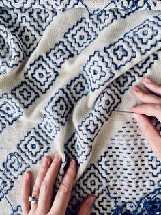 two hands on a blue and white blanket with some yarn next to it, while someone is knitting