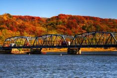 a train crossing a bridge over a body of water with fall colored trees in the background