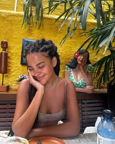 a woman sitting at a table in front of a yellow wall with two figurines behind her