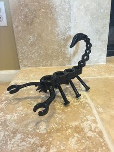 a black metal scorpion sculpture sitting on top of a tile floor next to a wall