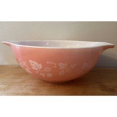 a pink and white bowl sitting on top of a wooden table next to a wall