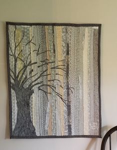 a wooden chair sitting next to a wall hanging with a tree on it's side