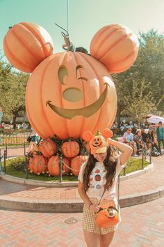 a woman standing in front of a giant pumpkin with a mouse face on it's head