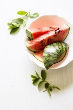 watermelon slices and leaves in a bowl on a white surface with green leaves