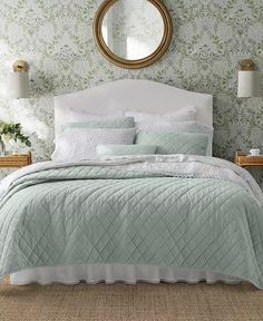 a bedroom with green wallpaper and white bedding in the corner, along with a round mirror on the wall