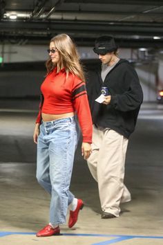 a man and woman are walking together in an empty parking garage, one is wearing red shoes