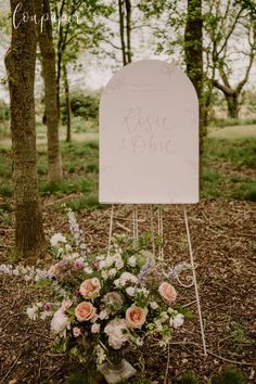 a wedding sign with flowers and greenery on it in front of some trees at the park