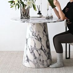 a woman sitting at a table reading a book with flowers in vases behind her