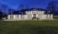 a large white house with lots of windows and lights on it's front lawn