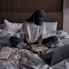 a person sitting on top of a bed with a laptop computer and book in front of them