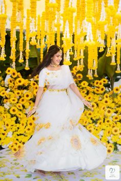 a woman in a white and yellow dress is walking through sunflowers with her hand on her hip