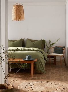 a bed with green sheets and pillows next to a wooden table in a white room