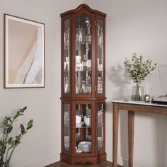 a tall wooden china cabinet with glass doors on the top and bottom, next to a table