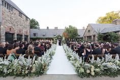 an outdoor wedding ceremony with white flowers and greenery at the end of the aisle