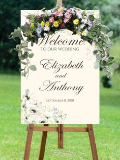 a welcome sign with flowers and greenery is displayed in front of a grassy field