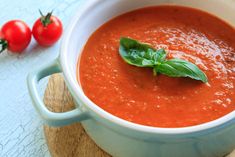 a bowl of tomato soup with basil on the top and tomatoes in the back ground