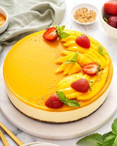 a cheesecake topped with sliced strawberries on top of a white plate next to bowls of fruit