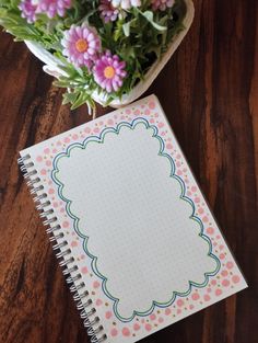 a notepad and flowers on a wooden table next to a potted plant with polka dots