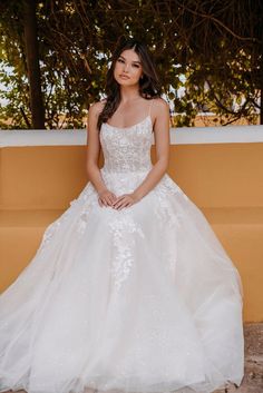 a woman in a white wedding dress sitting on a bench with her hand on her hip