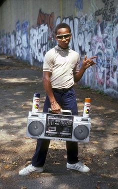 a man standing in front of a wall with graffiti on it holding a boombox