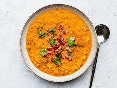 a white bowl filled with carrot soup and garnished with cilantro leaves