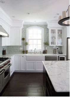 a white kitchen with marble counter tops and stainless steel stove top oven, dishwasher, and sink