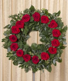 a wreath with red roses and greenery in front of a beige curtained background