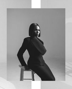 a black and white photo of a woman sitting on a stool with her hands on her hips