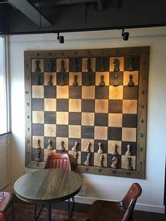 a wooden chess board mounted to the wall next to a table with chairs around it