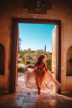 a woman in a dress is walking out of an open door with her hair blowing in the wind