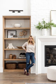 a woman standing in front of a book shelf next to a fire place and fireplace