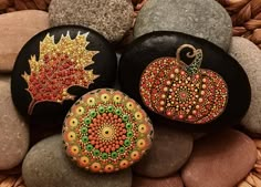 three painted pumpkins sitting on top of rocks next to each other with autumn leaves