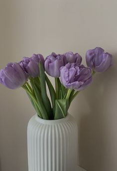 a white vase filled with purple flowers on top of a table