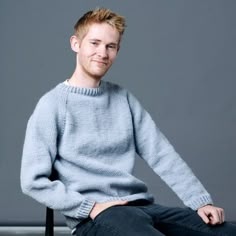 a young man sitting on top of a chair wearing a blue sweater and black jeans