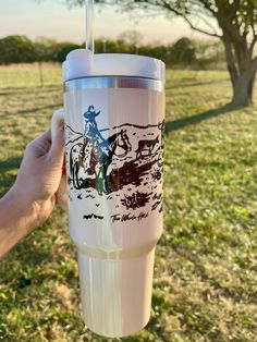 a person holding up a cup with a drawing on it in front of a field