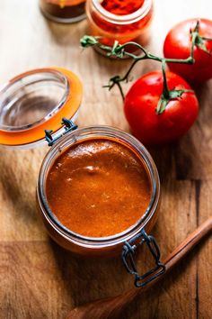 three jars filled with sauce sitting on top of a wooden cutting board next to tomatoes