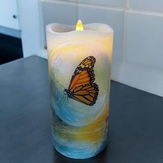 a lit candle with a butterfly painted on it