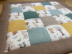 a quilted blanket with animals and trees on it in the middle of a floor